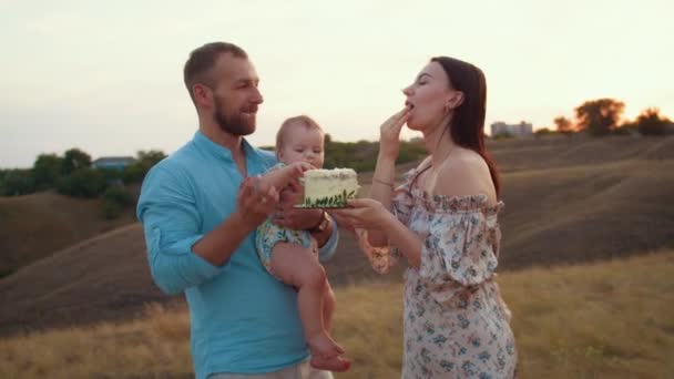 šťastná rodina s dítětem slaví první rok, jíst dort v poli při západu slunce, podzim a životní styl - Záběry, video