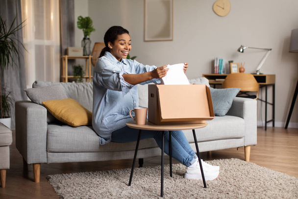 Pregnancy Shopping. Joyful Pregnant Black Woman Unpacking Delivered Box With New Clothes Sitting In Modern Living Room At Home. Delivery Offer And Ecommerce Concept - Fotoğraf, Görsel