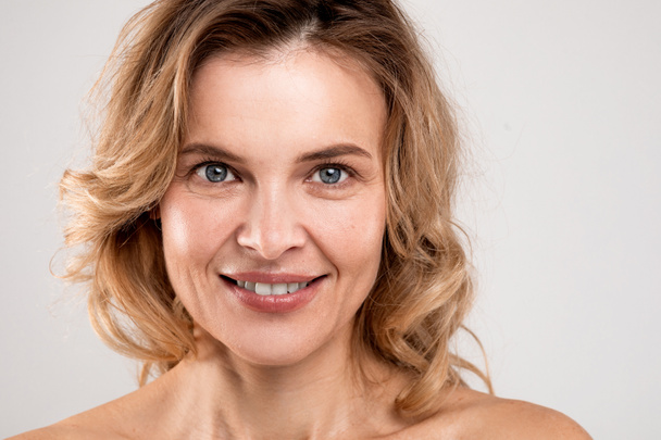 Closeup Portrait Of Smiling Attractive Middle Aged Woman With Bare Shoulders Posing Over Light Studio Background, Happy Mature Lady With Beautiful Aged Skin Looking At Camera, Copy Space - Photo, image