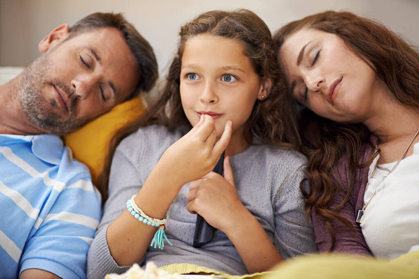 Family movie night. a girl sitting on the living room watching a movie with her parents asleep beside her - Foto, Bild