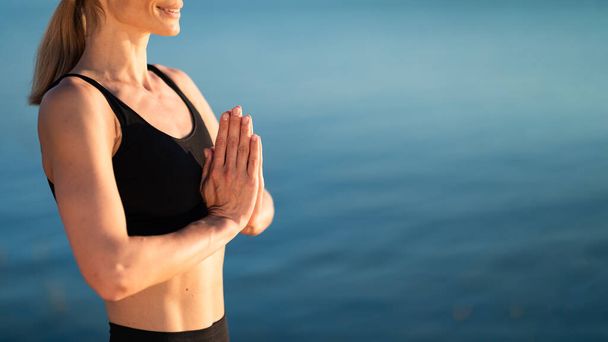 Cropped Shot Of Athletic Female Making Namaste Gesture While Practicing Yoga Outdoors, Calm Smiling Woman Meditating Outside, Standing With Clasped Hands Near River Or Sea, Panorama With Copy Space - Foto, Bild