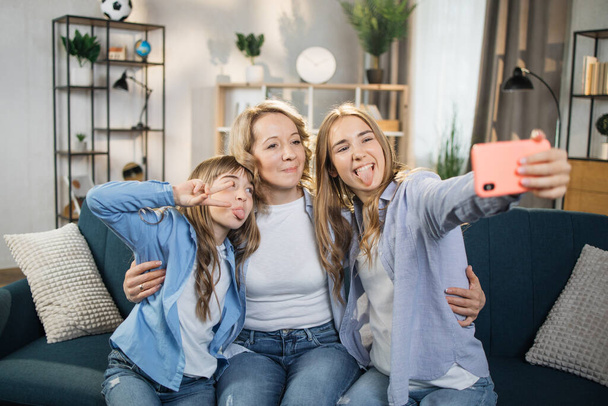 Head shot portrait close up smiling two daughters with mother taking selfie using smart phone, showing their tongues, happy mom with adorable kids making video call or recording vlog - Valokuva, kuva