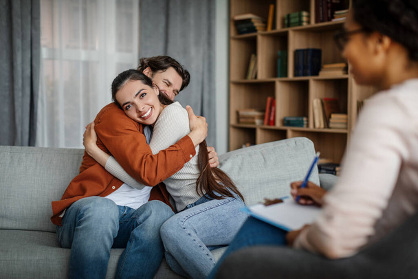 Glad millennial european male and female hugging at meeting with psychologist in office clinic interior. Great result, family psychological therapy, mental treatment together and professional help - Fotoğraf, Görsel