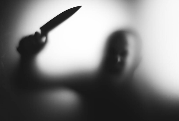 Horror, halloween background - Shadowy figure behind glass holding a knife - Фото, изображение
