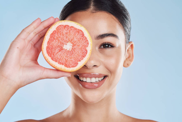 Portrait of woman with happy face and grapefruit in blue studio background. Her skincare and wellness beauty routine keeps her body fresh or healthy dental hygiene and clean smile or white teeth. - Foto, Bild
