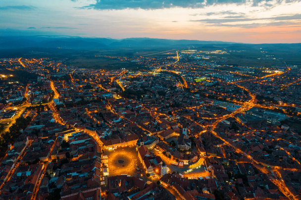 Aerial drone view of the Historic Centre of Sibiu at evening, Romania. The Great Square with Sibiu Lutheran Cathedral and old buildings around, narrow streets, people, illumination - Fotografie, Obrázek