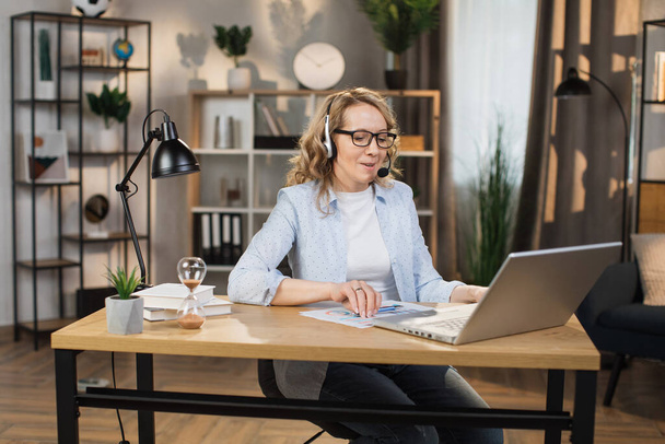 Confident mature woman typing on laptop at office or home, remote work. Caucasian female worker sitting at table with opened laptop, having video call. - Valokuva, kuva