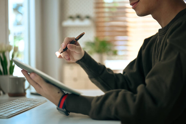 Чоловік фрілансер тримає ручку і використовує цифровий планшет під час роботи в Інтернеті з дому
. - Фото, зображення