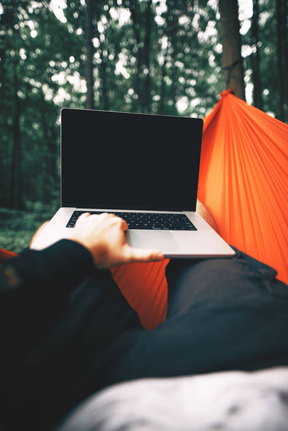 a man sitting with a laptop in the park. concept of modern people and digital nomad smart working job activity outdoors. POV using a laptop in the forest - 写真・画像
