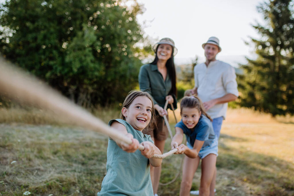 A young family with happy kids having fun together outdoors pulling rope in summer nature. - Foto, imagen