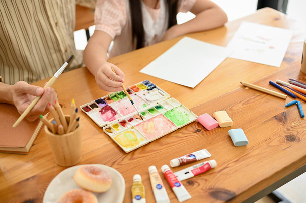 An Asian dad and daughter painting with a watercolor together at home. Happy family time, fun creative activity for kids. cropped and above view image  - Foto, afbeelding