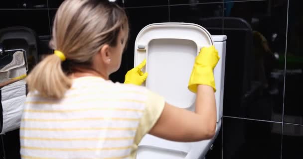 Woman is cleaning toilet seat with pink cloth and wiping toilet. Woman in yellow rubber gloves sitting and cleaning bathroom - Imágenes, Vídeo