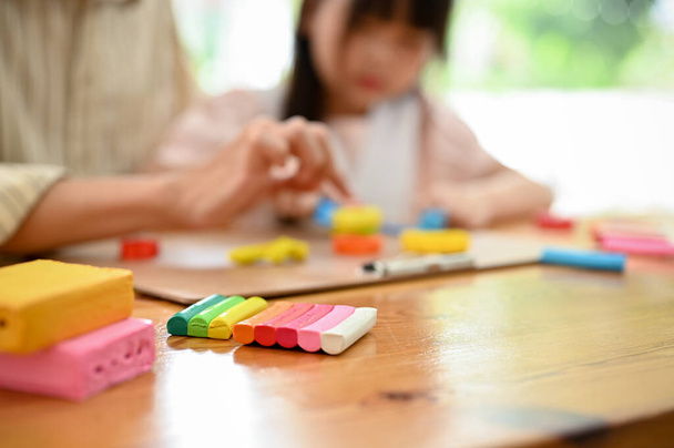 Colorful plasticine or play dough on a table over blurred background of dad and daughter playing and moulding play dough together. cropped and close-up image - Foto, immagini