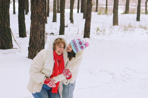 雪の公園、森林で面白い家族の肖像画。若い女性は、少女と彼女の母親は雪の近くに座って松の木を覆った。ピクニックだ。コーヒーを飲む。楽しんでるよ。冬休み - 写真・画像
