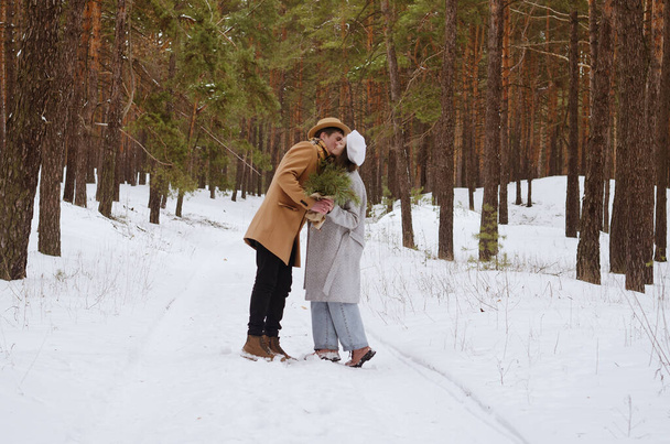 Portrait of funny family, couple in snowy park, forest. Young woman, girl and man in hat walking near snow covered pine trees. Drinking coffee. Having fun. Family winter holidays and date. Love - Foto, Imagem