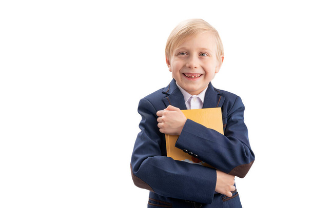 Smiling first-grader in school uniform hugs a book. Portrait of happy schoolboy with book. Isolation on white background - Фото, зображення
