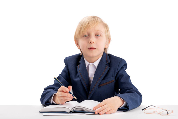 Diligent schoolboy sits at a desk with a pen and listens attentively to the teacher. First grader in class. Education concept. - Fotoğraf, Görsel