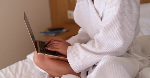Freelance blogger woman working on laptop while sitting on bed in bathrobe. Telework business mail check and remote work - Metraje, vídeo