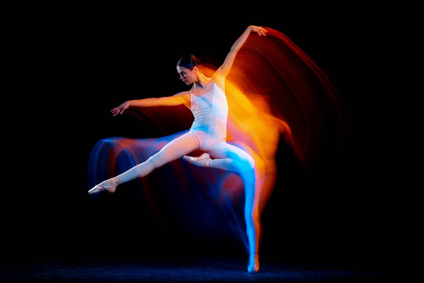 Dynamic portrait of tender slim girl, female ballet dancer in art performance isolated over black background in mixed bright neon light. Art, motion, action, flexibility, creativity and ad concept. - Foto, Imagem
