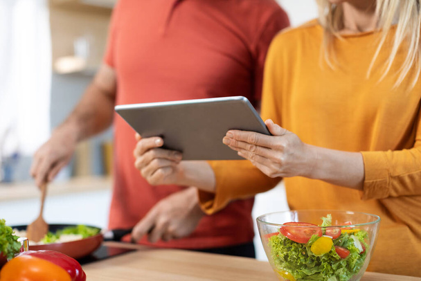 Unrecognizable couple cooking healthy dinner or lunch together at home, checking recipes online, using digital tablet, reading culinary blog on Internet, cropped, copy space - Foto, Imagem