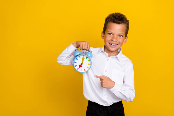 Portrait of positive cute boy indicate finger hand hold classic clock isolated on yellow color background. - Φωτογραφία, εικόνα