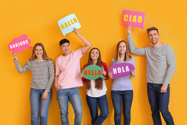 Group of young people holding speech bubbles with words HELLO in different languages on yellow background - Foto, Bild