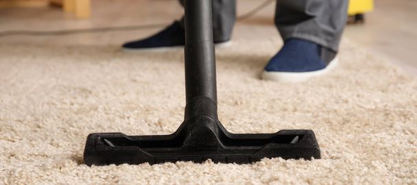 Man vacuuming carpet in room, closeup - Фото, изображение