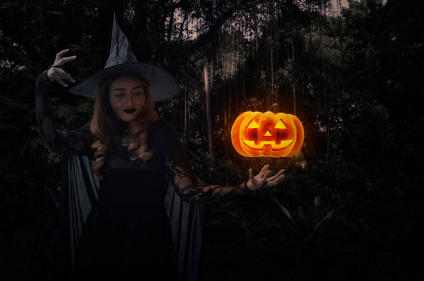 Halloween witch with pumpkin monster head standing over dark forest and tree, Halloween mystery concept - Fotó, kép