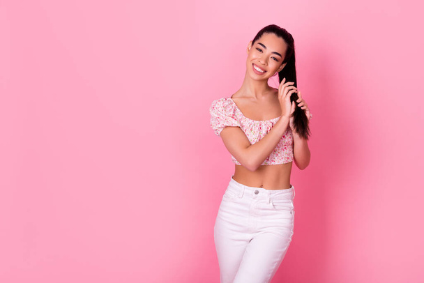 Photo of lovely millennial brunette lady hold hair wear crop top jeans isolated on pink color background. - Foto, immagini