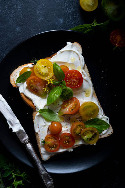 Cream cheese toast with cherry, colorful tomatoes. Black, moody background. Top view - Fotoğraf, Görsel