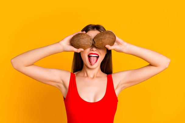 Photo of adorable funky woman wear swimsuit holding coco nuts close eyes showing tongue isolated yellow color background. - Фото, зображення
