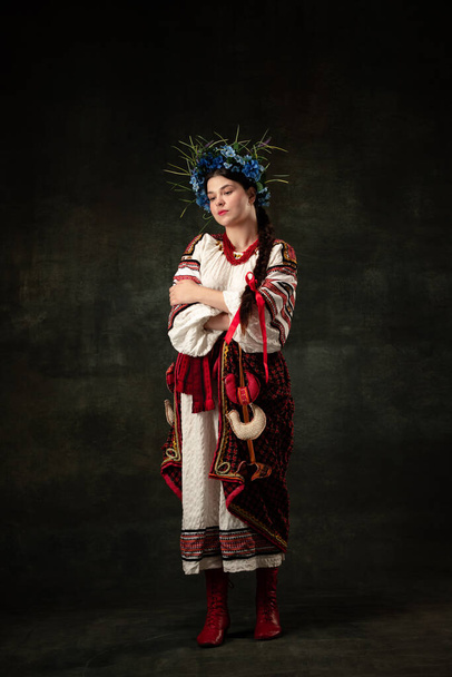 Sadness. Art portrait of beautiful woman wearing traditional folk Ukrainian costume posing isolated over dark vintage background. Fashion, beauty, cultural heritage concept. - Photo, Image