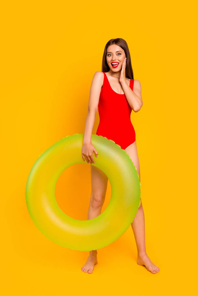 Full body vertical portrait of astonished gorgeous girl hold inflatable ring hand touch cheek isolated on yellow color background. - Fotó, kép