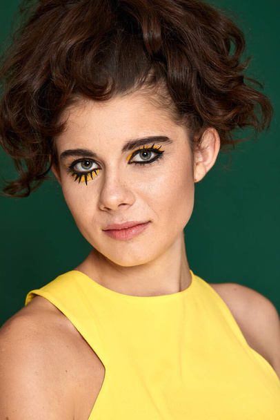 young curly woman with creative make-up in yellow dress on green background. - 写真・画像
