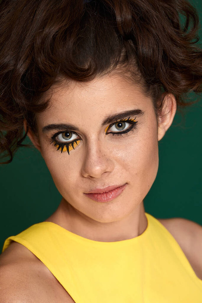 young curly woman with creative make-up in yellow dress on green background. - Φωτογραφία, εικόνα