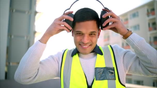 Building construction, man and safety ear headphones for happy, smile and motivation worker or engineering employee. Portrait of industrial architect with property vision for real estate architecture. - Video, Çekim