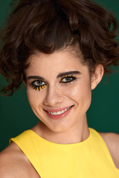 young curly woman with creative make-up in yellow dress on green background. - Foto, immagini