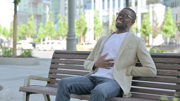 afroamericano uomo avendo indietro dolore mentre seduta su panchina all'aperto - Foto, immagini