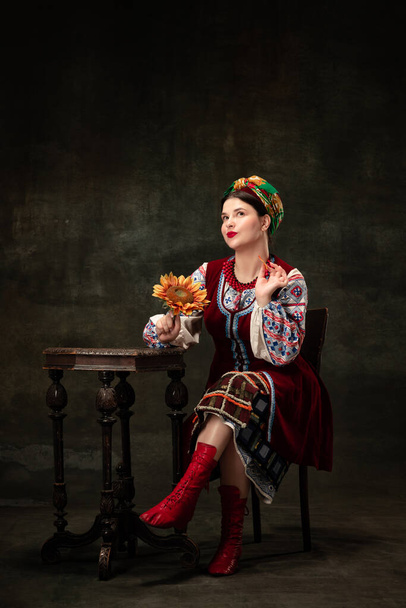 Emotional young woman wearing national folk Ukrainian attire isolated over dark retro background. Human emotions, history, ad, fashion, beauty, eras comparison concept. - Valokuva, kuva
