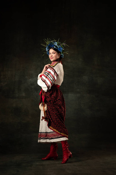 Freedom and independence. Art portrait of beautiful woman wearing traditional folk Ukrainian costume posing isolated over dark vintage background. Fashion, beauty, cultural heritage concept. - Foto, Imagem