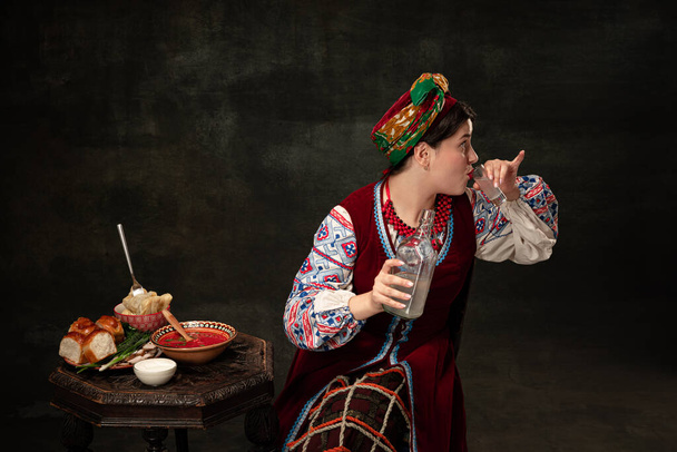 One young beautiful Ukrainian woman in traditional folk Ukrainian costume isolated over dark vintage background. Fashion, beauty, cultural heritage, eras comparison concept. - Valokuva, kuva