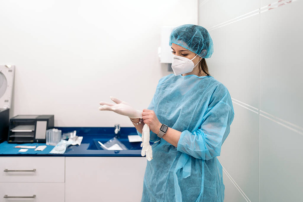 Female medical worker wearing face mask and protective clothes putting on latex gloves. - Photo, Image