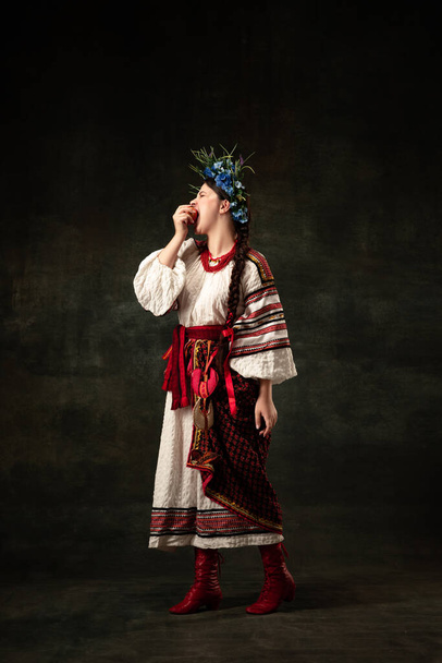 Freedom and independence. Art portrait of beautiful woman wearing traditional folk Ukrainian costume posing isolated over dark vintage background. Fashion, beauty, cultural heritage concept. - Fotó, kép