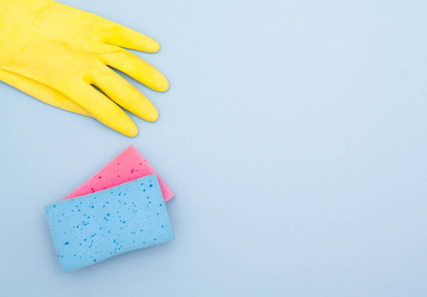 Синьо-рожеві кухонні губки з жовтими гумовими рукавичками на синьому з копіювальним простором
 - Фото, зображення
