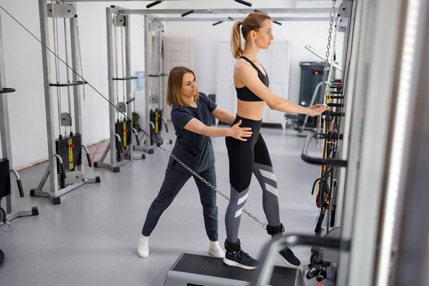 Woman doing exercise on decompression simulators with trainer rehabilitation. Sports physiotherapist assisting young female patient exercise therapy. Kinesitherapy technology  - Fotografie, Obrázek