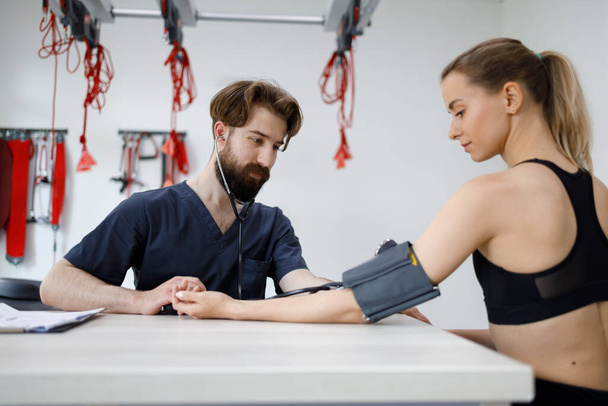 Doctor measures blood pressure in a young sports woman - Photo, Image