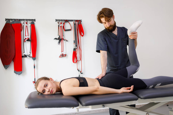 Female patient doing physical exercises with physiotherapist. Male rehabilitation specialist treating injured knee of athlete. Concept of post traumatic recovery - Foto, immagini
