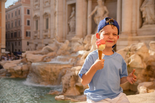 Cute cheerful boy 7 years old eating ice cream (gelato) near the Trevi Fountain in Rome, Italy. Traveling with children, family vacation, intellectual development of the child - Photo, image