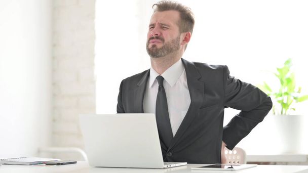 Бизнесмен с болями в спине при использовании ноутбука в офисе - Фото, изображение