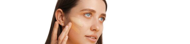 Cropped panorama photo of a woman face applying foundation cream on it and choosing the right color. - Фото, изображение